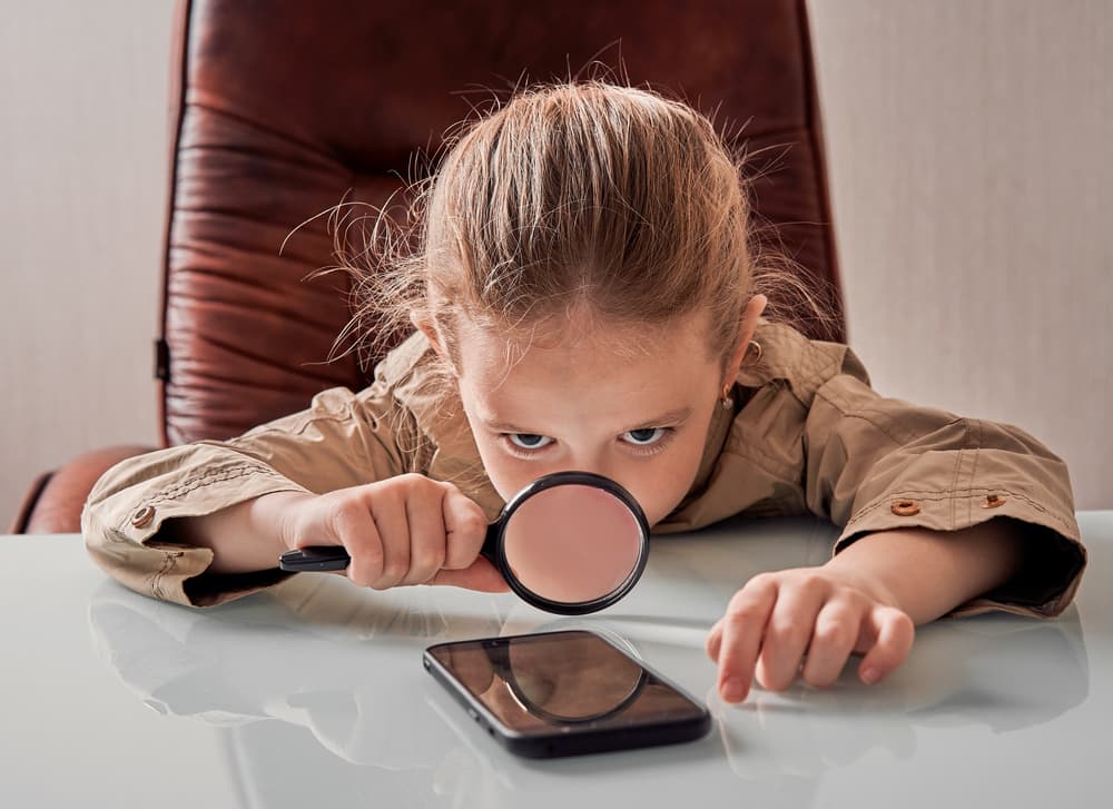 girl looking at smart phone through magnifying glass