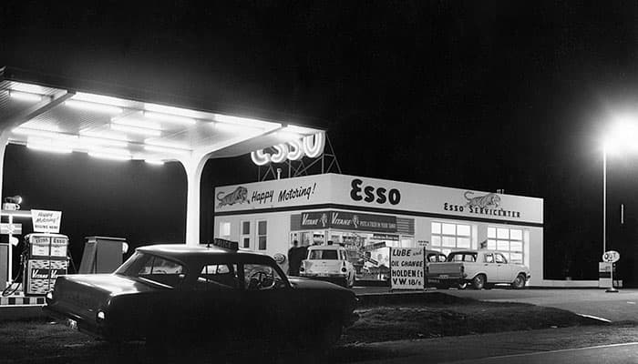 1964 image of an Esso service station at night with cars on the forecourt. Black and white.