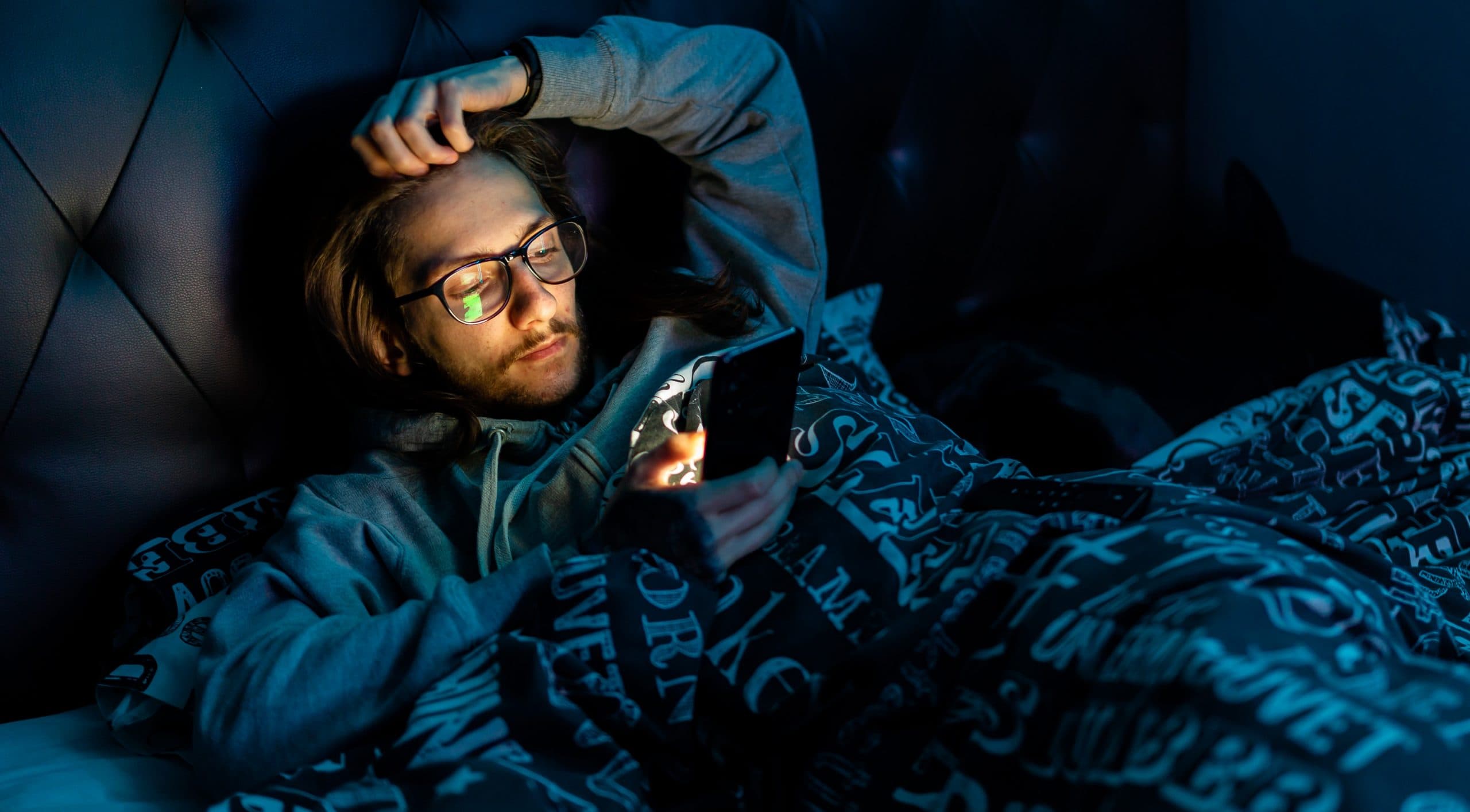 Young man in bed at night looking at his mobile phone restlessly.