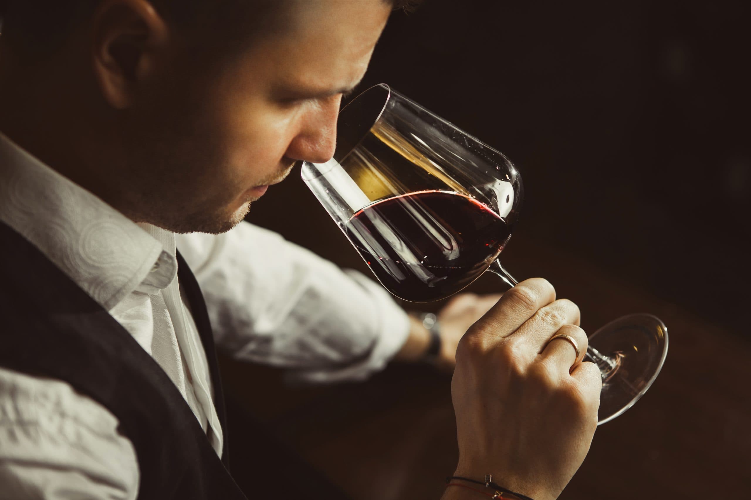 Close up shot of a young man, smelling a glass of Red wine.
