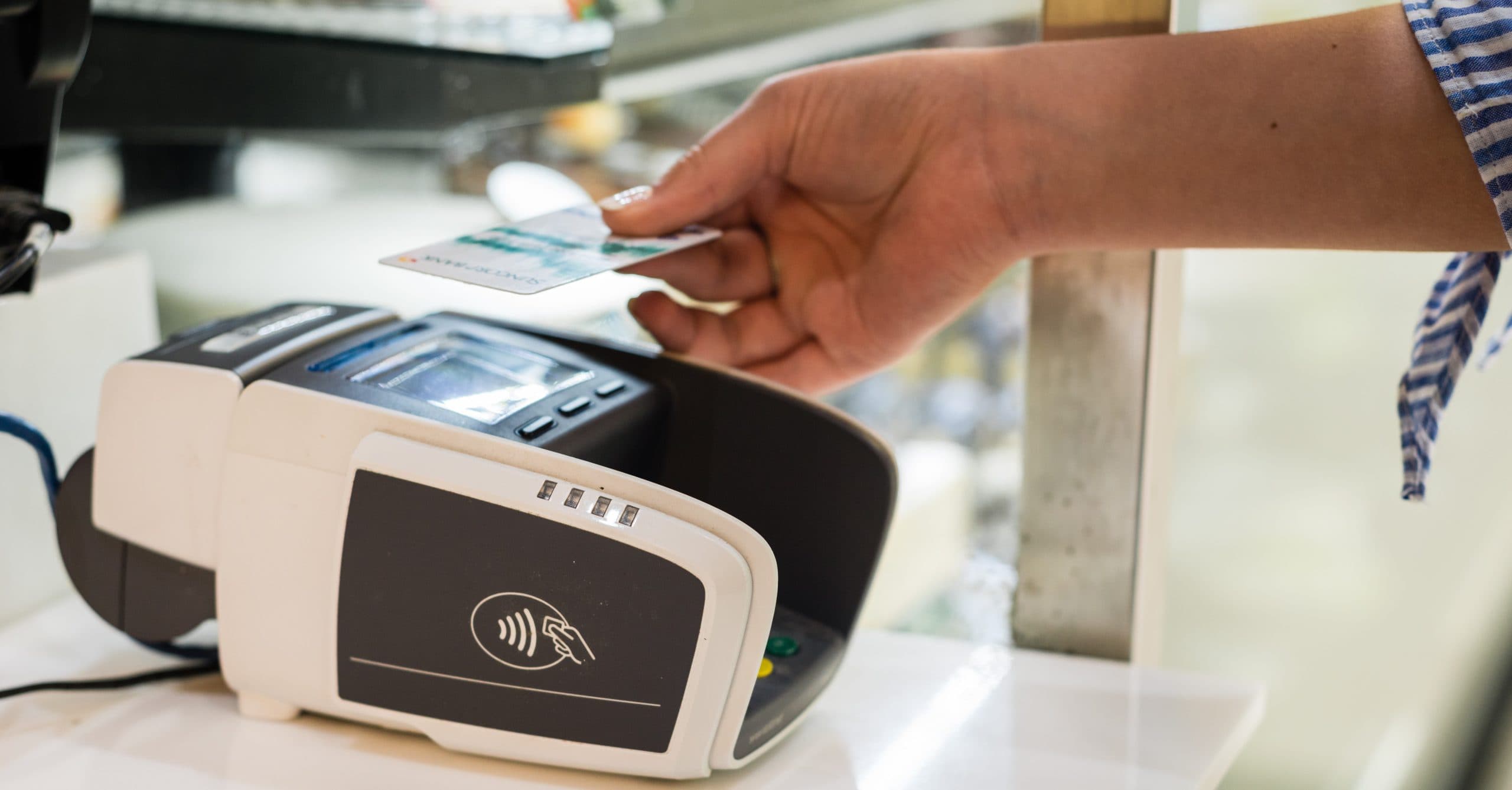 A person's hand holds a bank card over an eftpos machine on the counter in a store.