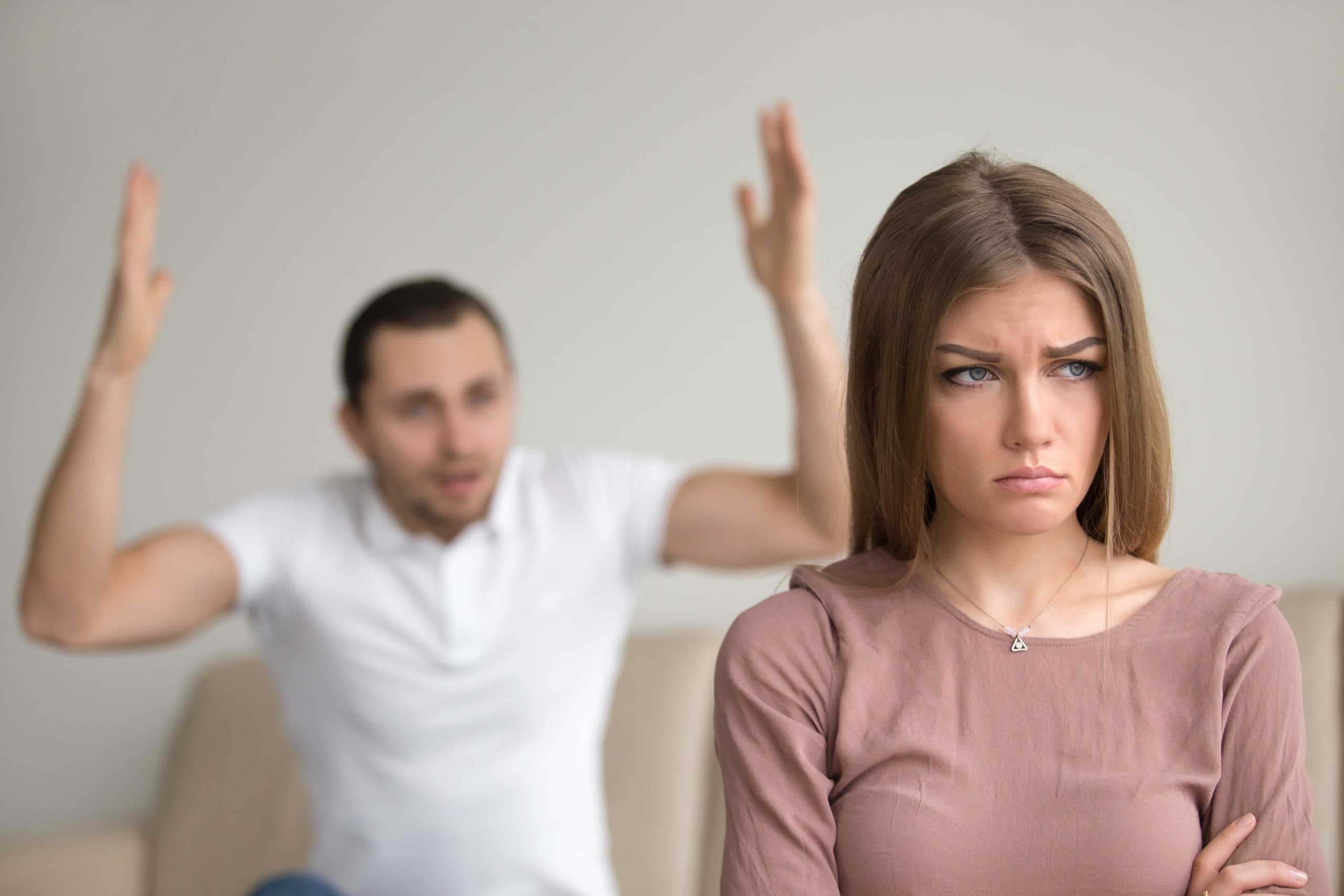image of a man in the background raising his hands and yelling, while a woman in front of him appears sad