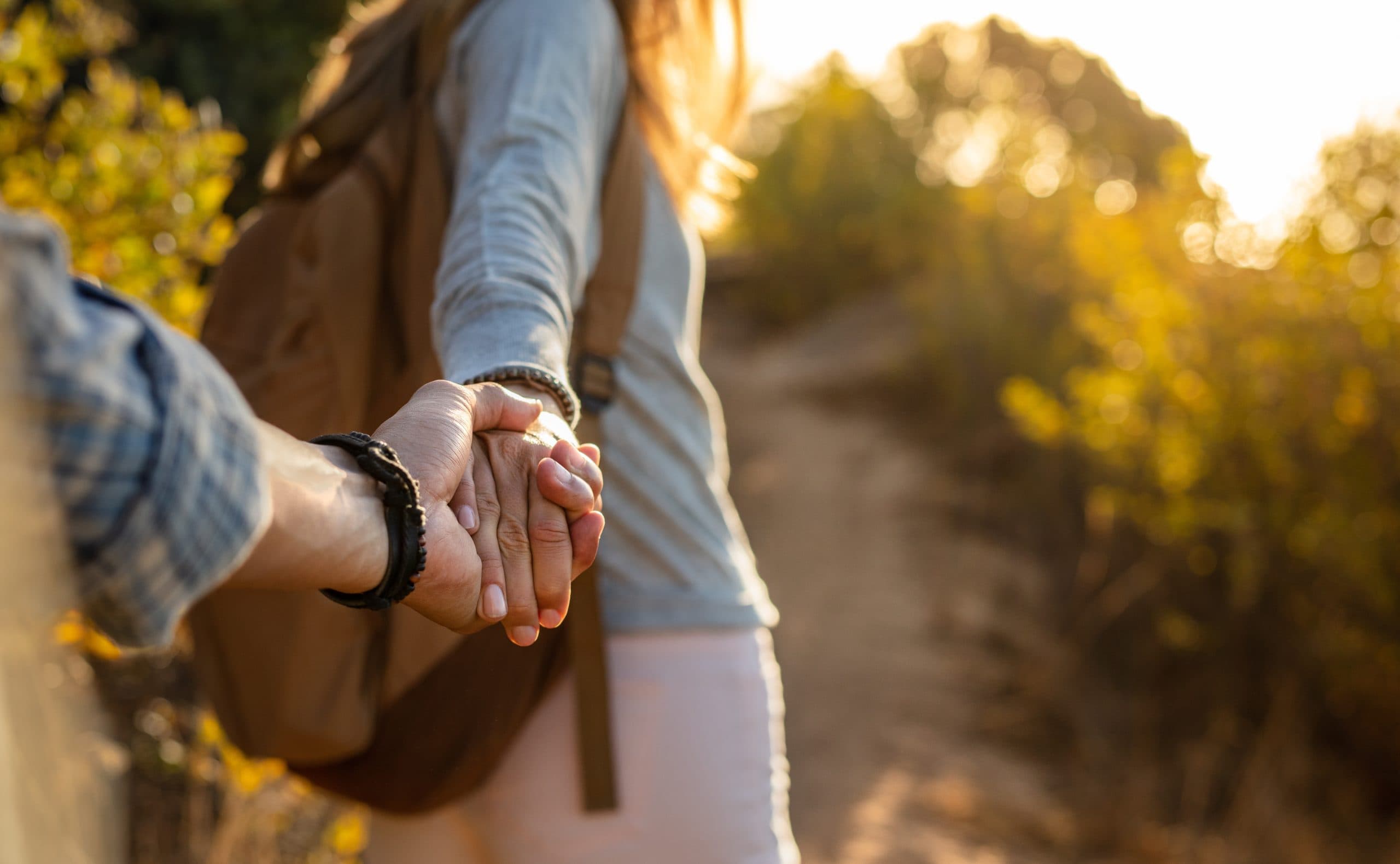 Close-up shot of the arms and hands of a young couple outdoors on a bushland walking trail.