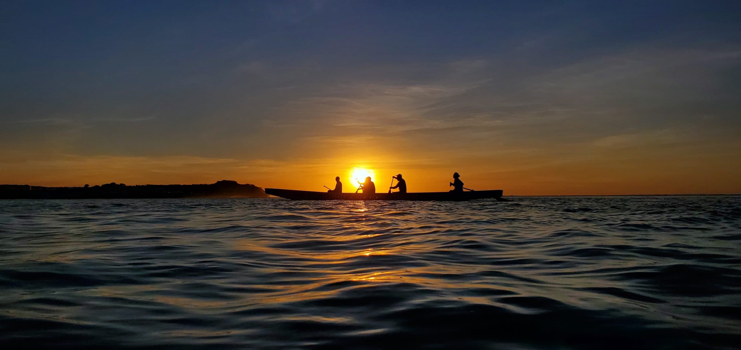 Silhouettes of four kayakers on the water at sunset in Guam.