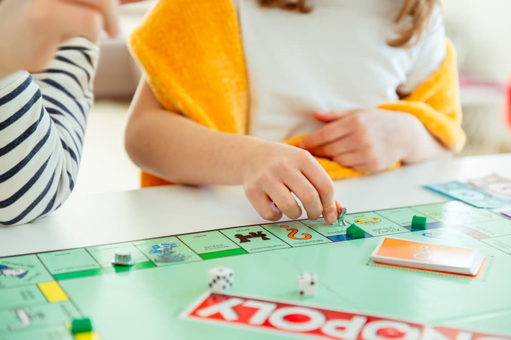 Hands of two children sitting around a Monopoly game board and moving pieces around.