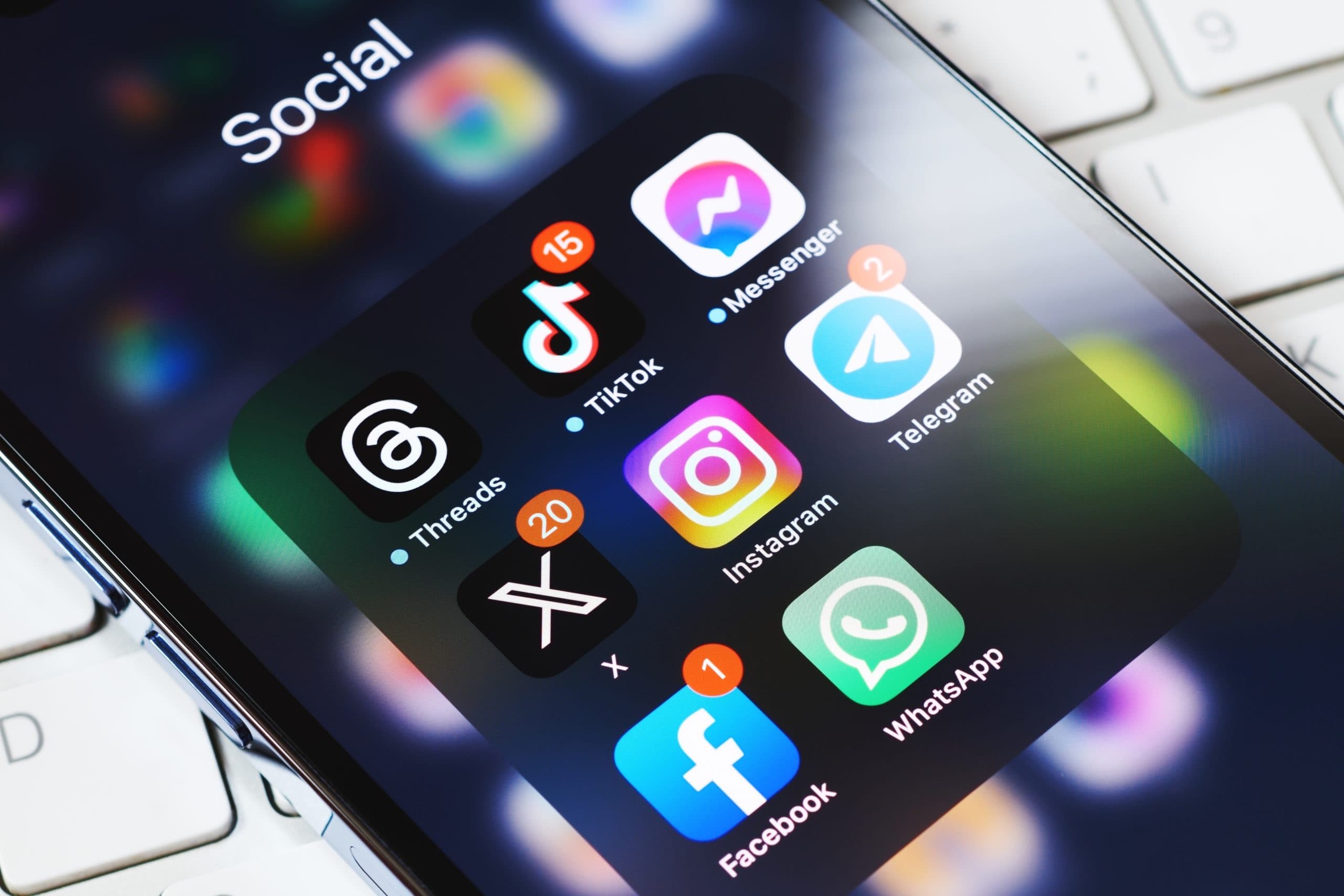 a smartphone screen with multiple modern social media apps - threads, tiktok, messenger, x/twitter, instagram, telegram, facebook and whatsapp - all in a folder under the title of 'social'