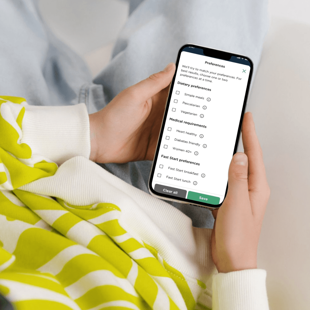 A young person in a bright hoodie holds a phone on their lap. We can see the CSIRO Wellbeing Diet app on the screen. The screen shows meal style preferences they are selecting to tailor their meal plan. (Image provided: CSIRO)