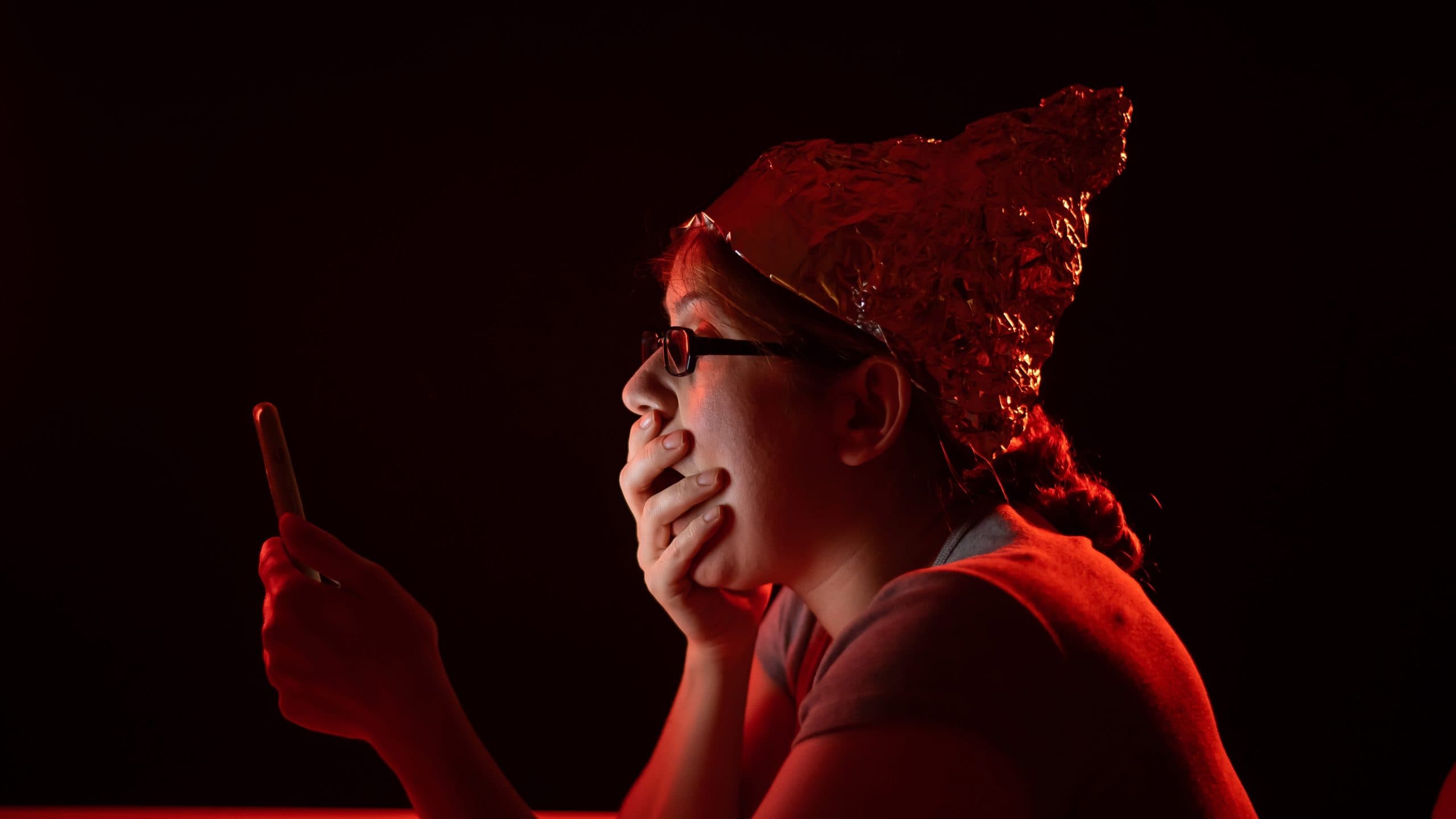 an image of a woman with a tin foil hat looking at her phone with her hand over her mouth