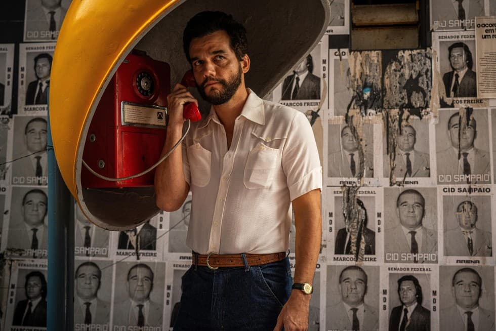 an image of walter moura - a tan skinned man in a white button down shirt - on a red phone in front of a collection of black and white wanted posters